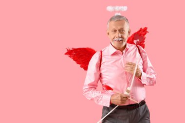 Aşk tanrısı gibi giyinmiş, kalbi olan ve pembe arka planı olan olgun bir adam. Sevgililer Günü kutlaması