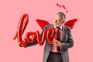 Aşk tanrısı gibi giyinmiş olgun bir adam pembe arka planda balonlardan yapılmış bir aşk sözcüğü. Sevgililer Günü kutlaması
