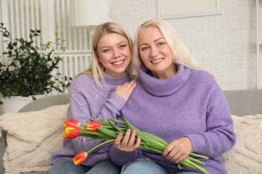 Evinde bir buket lale çiçeğiyle güzel bir kadın ve annesi var.