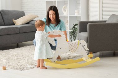 Evde annesi ve sallanan atı olan küçük bir kız bebek.