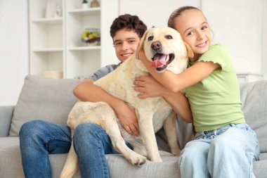 Mutlu kız ve erkek kardeş ve şirin Labrador köpeği evdeki kanepede oturuyor.