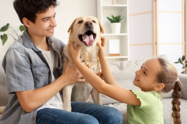 Mutlu kız ve erkek kardeş ve şirin Labrador köpeği evdeki kanepede oturuyor.