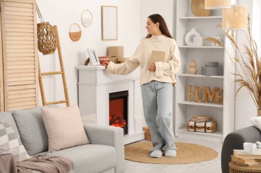 Evinde şöminenin yanında kitabı olan güzel, genç ve mutlu bir kadın.