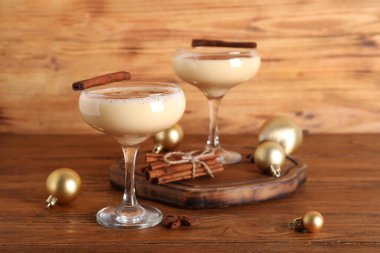 Tarçınlı nefis eggnog kokteyli ve ahşap arka planda Noel topları.