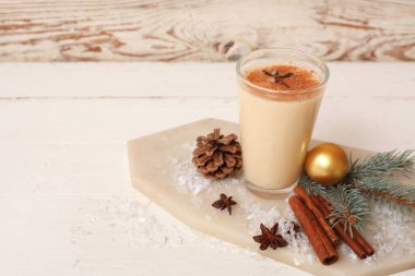 Yıldız anason, tarçın, köknar dalı ve beyaz ahşap arka planda noel balosuyla nefis bir eggnog kokteyli.