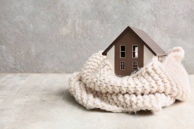 Gri arka planda sıcak eşarbı olan bir ev modeli. Isınma mevsimi kavramı