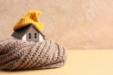 Bej arka planda sıcak atkısı ve şapkası olan ev modeli. Isınma mevsimi kavramı