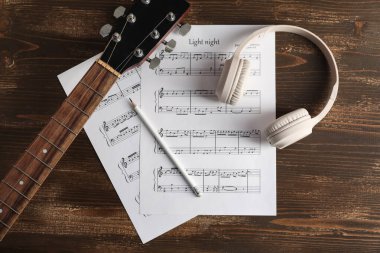 Müzik kağıtları, modern kulaklıklar, tahta arka planda kalem ve gitar.
