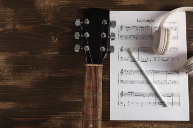 Müzik sayfası, modern kulaklıklar, tahta arka planda kalem ve gitar.