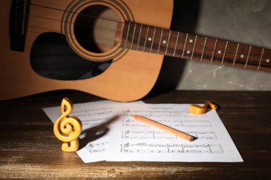 Müzik kağıtları, nota işaretleri, tahta masada kalem ve gitar.