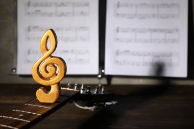 Gitar, keman anahtarı ve müzik kağıtları ahşap masada, yakın plan.