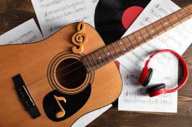 Gitar, nota işaretleri, nota kağıtları, kulaklıklar ve ahşap masadaki vinil disk.