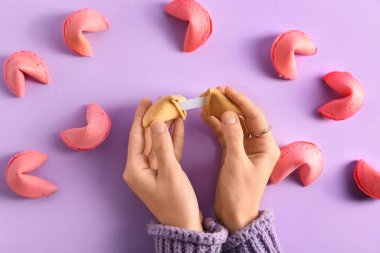 Leylak arka planında kırık fal kurabiyesi olan kadın elleri.