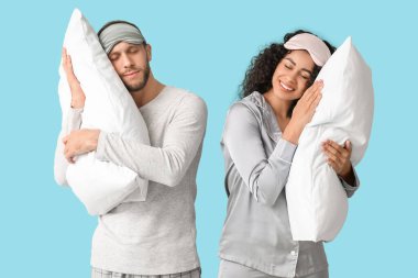 Mavi arka planda yumuşak yastıklı pijama ve maskeli güzel bir çift. Dünya Uyku Günü