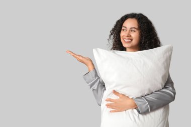 Gri arka planda yumuşak yastıklı pijamalı güzel bir Afro-Amerikalı kadın. Dünya Uyku Günü