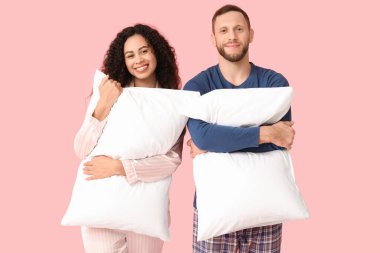 Pembe arka planda yumuşak yastıklı pijamalı güzel bir çift. Dünya Uyku Günü