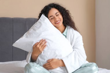 Yatak odasında yumuşak yastıklı pijamalı güzel bir Afro-Amerikalı kadın. Dünya Uyku Günü