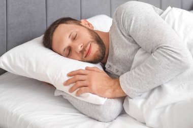 Yatak odasında pijamalı genç bir adam uyuyor. Dünya Uyku Günü