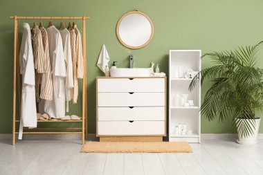 Giysilerle, çekmecelerle ve yeşil duvarın yanındaki raflarla dolu bir oda.