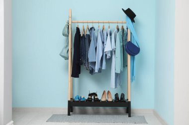 Mavi duvarın yanında giysi, ayakkabı ve aksesuarlarla dolu bir oda.