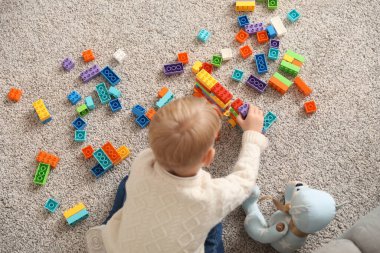 Sevimli küçük çocuk evde renkli oyuncak tuğlalarla ve oyuncak ayıyla oynuyor.