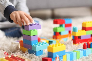 Evdeki halıda renkli oyuncak tuğlalarla oynayan sevimli küçük çocuk, yakın plan.