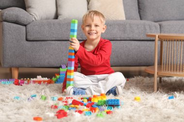 Mutlu küçük çocuk evde renkli oyuncak tuğlalarla oynuyor.