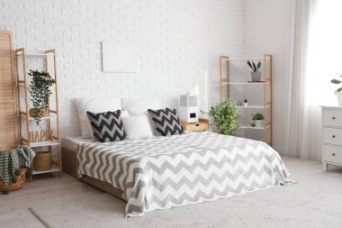 Yatak odasının içinde ev bitkileri ve beyaz tuğla duvarın yanındaki komodinin yanında nemlendirici var.