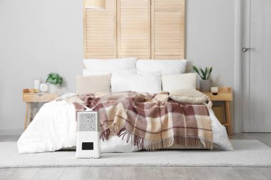 Yatak odasının içinde komodinlerin, ev bitkilerinin ve zeminde modern nemlendirici var.