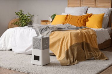 Yatak odasının içinde yatağın yanında modern nemlendirici var.