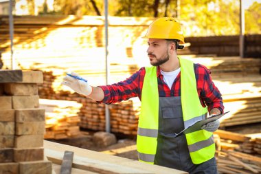 Yansıtıcı yelek giyen genç marangoz kereste fabrikasında çalışıyor.