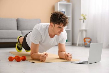 Modern dizüstü bilgisayarı ve dambılları olan sportif bir genç.