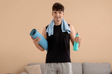 Evde bir şişe su ve yoga minderiyle sportif bir genç adam.