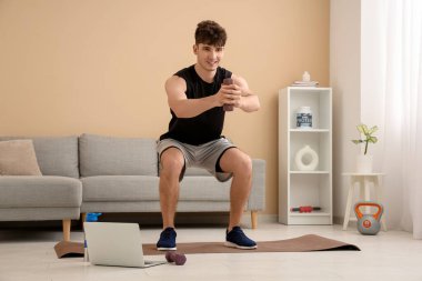 Modern dizüstü bilgisayarı ve dambılları olan sportif bir genç.