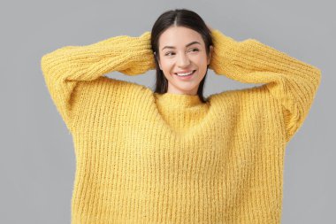 Gri arka planda gülümseyen güzel genç bir kadın.