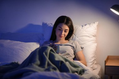 Geceleri yatağında cep telefonu olan güzel genç bir kadın.