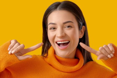 Güzel, genç, mutlu, gülümseyen bir kadın sarı arka plandaki gülüşünü gösteriyor.