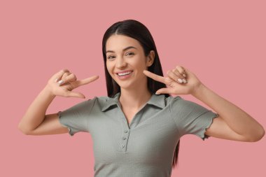 Güzel, genç ve mutlu bir kadın pembe arka plandaki gülüşünü işaret ediyor.