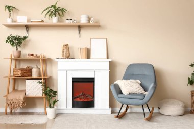 Şömineli oturma odası, raf ünitesi ve bej duvarın yanındaki gri sallanan sandalye.