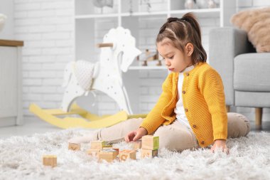 Küçük şirin kız tahta küplerle oynuyor ve oturma odasında halının üzerinde oturuyor.