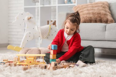 Küçük şirin kız tahta küplerle oynuyor ve oturma odasında halının üzerinde oturuyor.