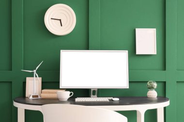 Ofiste yeşil duvarın yanında rüzgar türbini modelli boş bilgisayar monitörü.