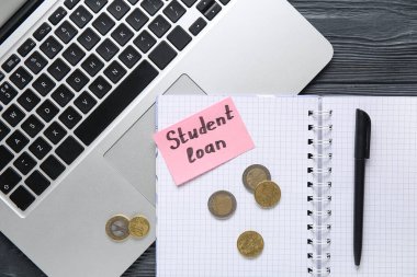 Koyu ahşap zemin üzerinde SÜDENT kredisi, kalem, bozuk para ve modern dizüstü bilgisayarlı defter, yakın plan