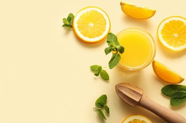 Sarı zemin üzerinde nane ve ahşap sıkacağı olan bir bardak taze portakal suyu.