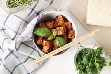 Kızarmış tofu peyniri ve beyaz arka planda bitkilerle dolu bir kase.