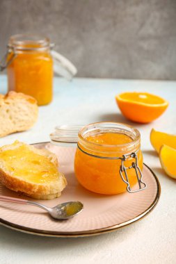 Açık mavi masada bir tabak ekmek ve bir kavanoz tatlı portakal reçeli.