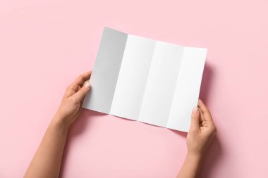 Pembe arka planda boş broşürleri olan kadın elleri.