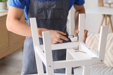 Male carpenter tightening screw in white wooden furniture with screwdriver clipart