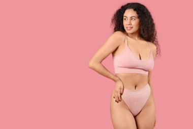 Pembe arka planda zarif iç çamaşırlı güzel, mutlu, Afro-Amerikan kadın.