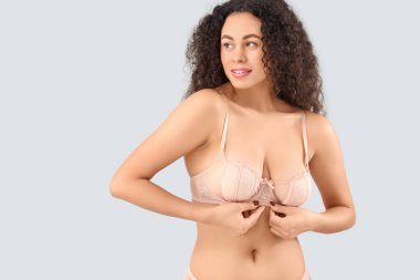 Gri arka planda zarif pembe iç çamaşırlı güzel, mutlu, Afro-Amerikan kadın.